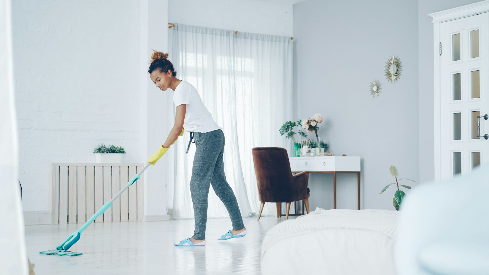 A cleaner in gloves mops the floor of a bright, modern living room