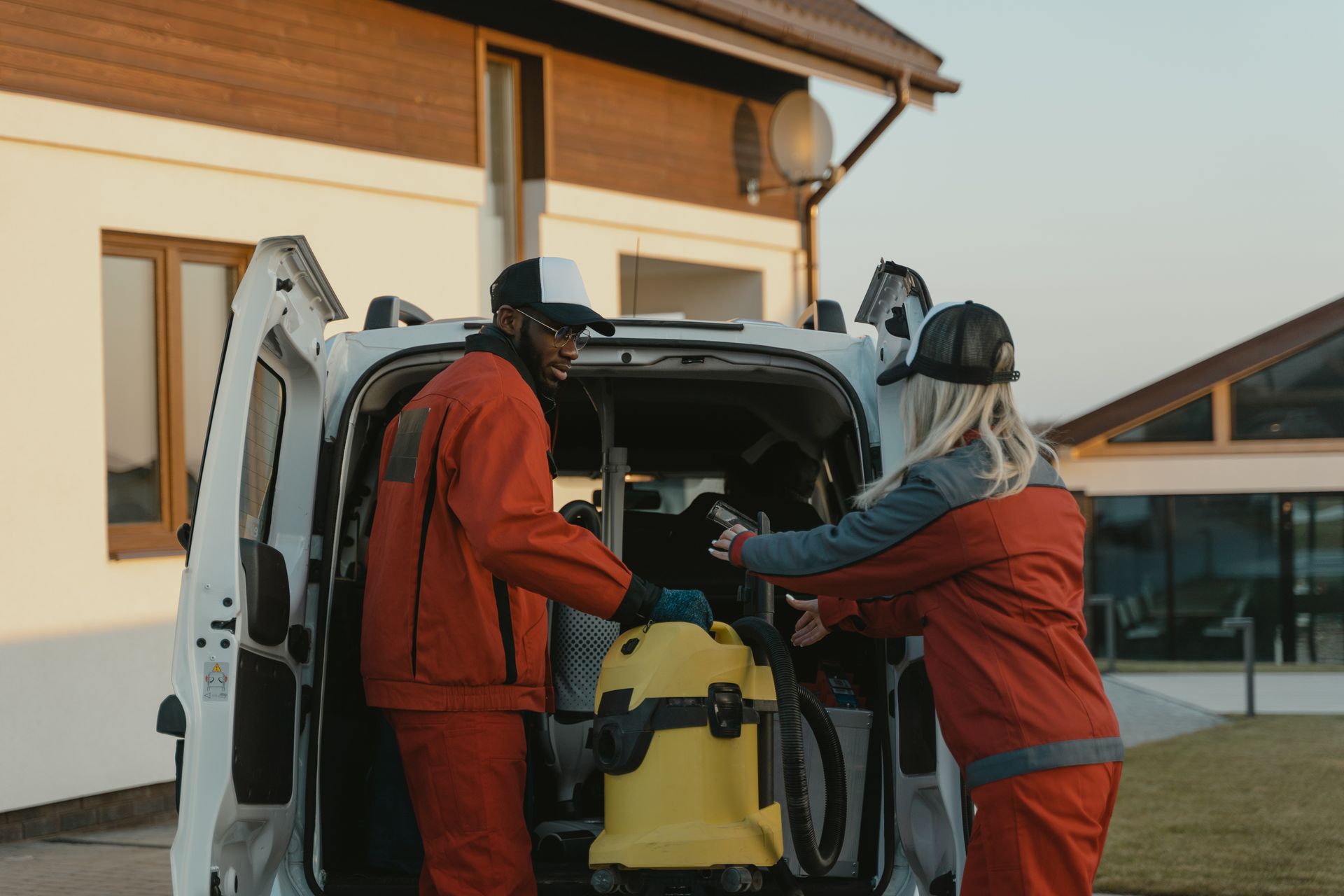 Two cleaners in uniform load a vacuum cleaner into a white van